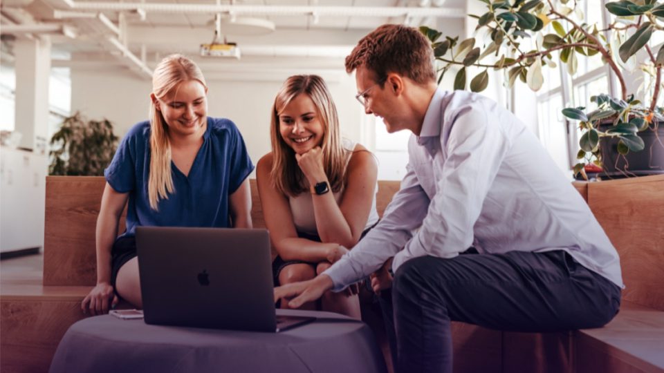 Drei Personen sitzen an einem Laptop